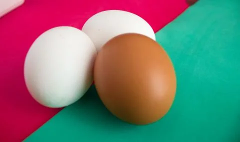 Three chicken eggs on table with green, turquoise and red background Stock-Fotos