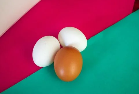 Three chicken eggs on table with green, turquoise and red background. Stock Photos