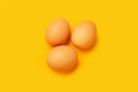Three chicken eggs on a yellow background Stock Photos