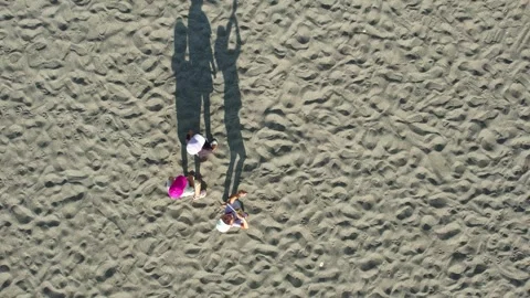 Three children in baseball caps cast long shadows on a sandy beach, drone Video stock 256571879