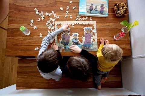 Three children, boys, assembling puzzle with their picture from the beach, pl Stock Photos