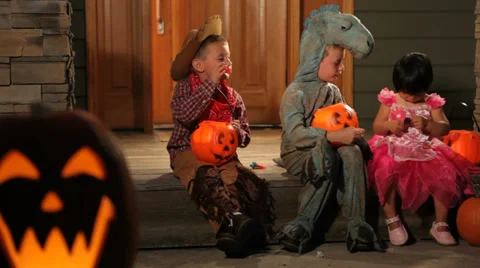 Three children in Halloween costumes sitting on porch Stock Footage