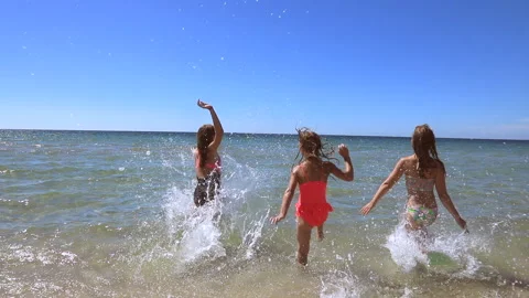 Three children having fun on a beach running to the seasea Stock Footage 153108611