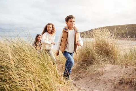 Three Children Having Fun Exploring In Sand Dunes On Winter Beach Vacation Stock Photos