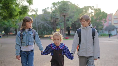 Three Children Holding Hands Walking Together Through City Park in Afternoon. Vídeo Stock 338141038