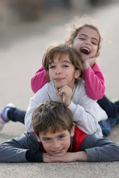 Three children lying on the floor one on top of the other. Stock Photos