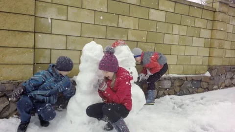 Three children make a snowman. Snowing. Video stock 74870158