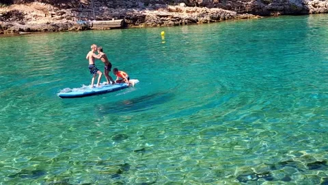 Three children play on a SUP board, pushing each other 스톡 동영상 315671886