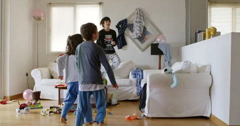 Three children playing and jumping on a couch in a cluttered living room during Stock Footage 274826948