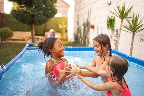 Three children playing with a ball in a backyard swimming pool Stock Photos