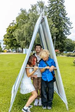 Three children playing inside a triangular wooden structure in a park, one .. Stock Photos