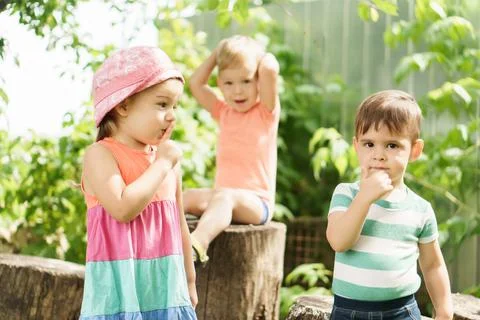 Three children of same age show different emotions. Kids in green garden play Foto stock