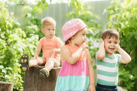 Three children of same age show different emotions. Kids in green garden play Foto stock