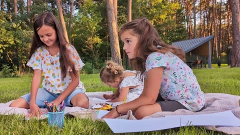Three children sit on a blanket in a park, drawing and coloring with crayons and Stock Footage 341490819