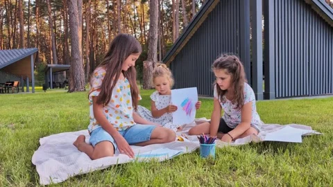 Three children sit on a blanket in a park. They draw and color with crayons Stock Footage 341490836