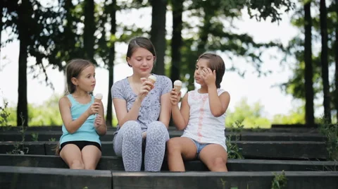 Three children sitting on a bench in the park and eat ice cream Stock Footage 65779747