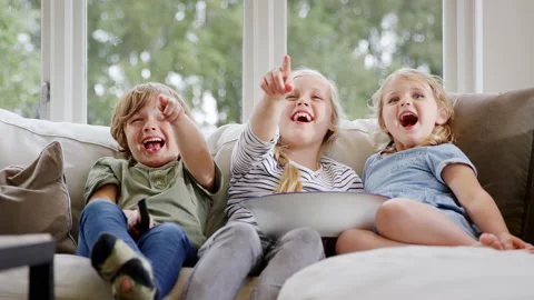 Three Children Sitting On Sofa At Home Laughing And Watching TV With Popcorn Stock Footage 147361004