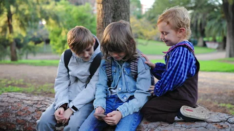 Three Children Sitting on Tree Log in Park Looking at Smartphone Together. Vidéo 338140150