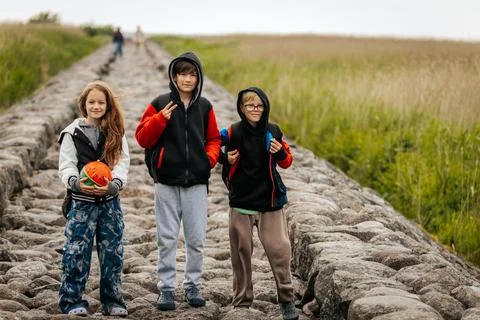 Three children stand on a stone path in nature, smiling and posing casually Stock Photos