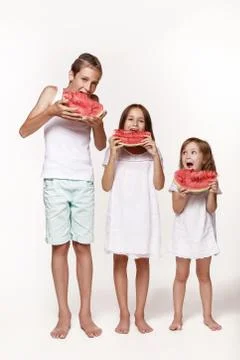 Three children in the studio stand on a white background and eat pieces of wa Stock Photos