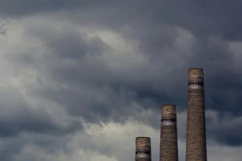 Three chimneys of a machine-building enterprise against a gloomy sky backgrou 스톡 사진