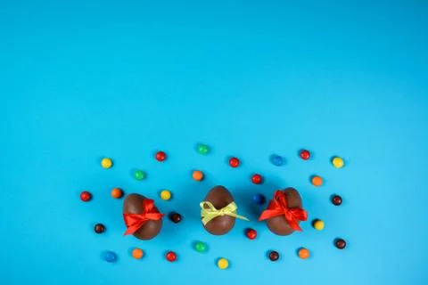 Three chocolate Easter eggs among colorful dragee on the blue background. Cop Stock Photos