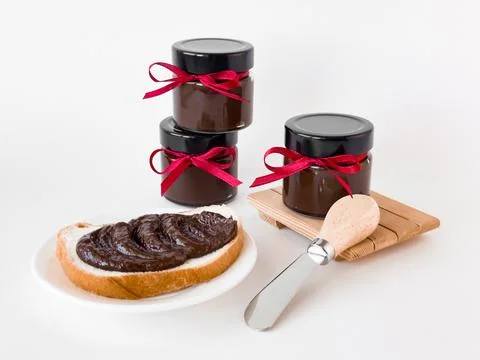 Three chocolate spread jars with red ribbons and toast on white background Foto stock
