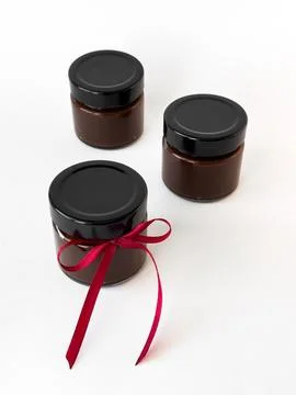 Three chocolate spread jars on white background with red ribbon accent Foto stock