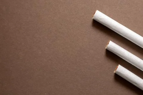 Three cigarettes lined up on a brown background. Area left for copyspace Stock Photos