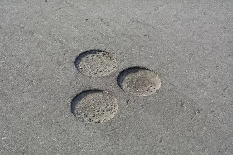 Three circular core drill marks in gray concrete pavement show surface traces Фото