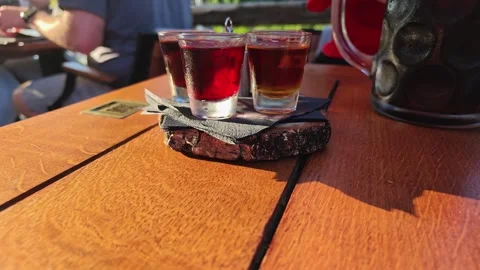 Three clear glasses of amber and ruby beverages on bark coaster beside sunlit Video stock 343628314