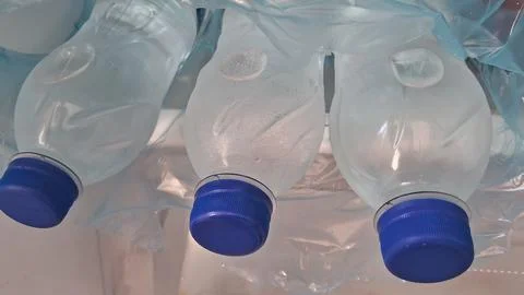 Three clear plastic water bottles with blue caps inside plastic Stock Photos