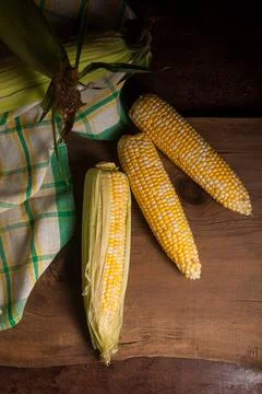 Three cobs sweet corn with green leaves on wooden background.. Stock Photos