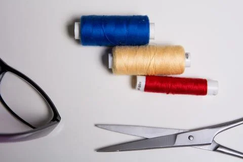 Three coils of multicolored threads, glasses and scissors Stock Photos