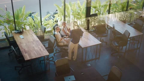 Three colleagues are discussing work in modern coworking space with wooden desks Stock Footage 312123077
