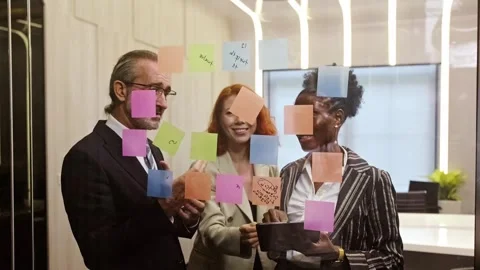 Three colleagues brainstorm in a modern office, placing colorful sticky notes Stock Footage 315675248