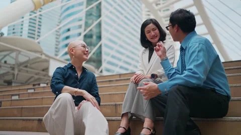 Three colleagues laugh while seated on city steps Stock Footage 348284095