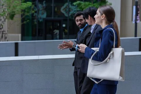 Three colleagues walking in profile point ahead while explaining an idea on.. Stock Photos
