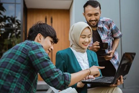 Three college students using and looking at laptop in cafe Stock Photos