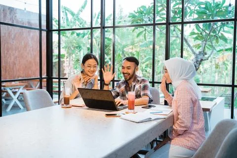 Three college students waving while meeting online using a laptop Stock Photos