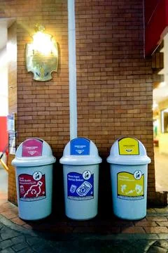 Three Color Coded Trash Bins for Waste Sorting Against Brick Wall Stock Photos