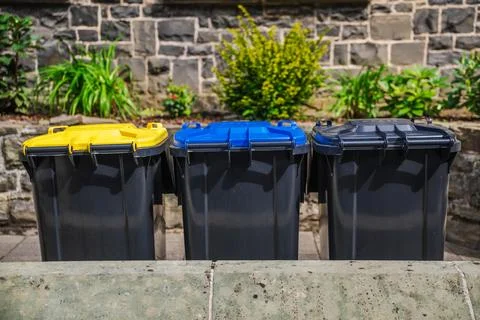 Three Color-Coded Waste Bins by Stone Garden Wall Stock Photos
