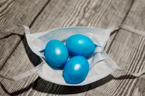 Three colored blue easter eggs laying in medical mask. Stock Photos