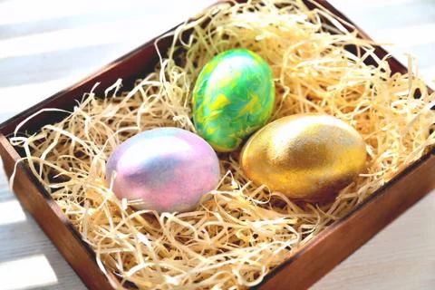 Three colored chicken eggs in a box with shavings in the sunlight Stock Photos