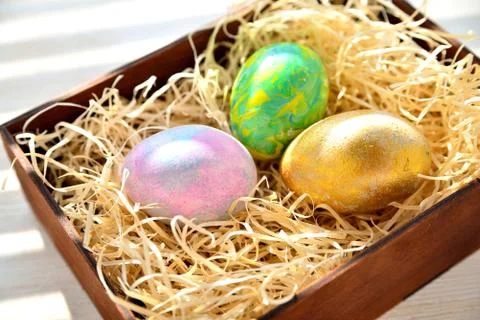 Three colored chicken eggs in a box with shavings in the sunlight Stock Photos