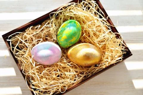 Three colored chicken eggs in a box with shavings in the sunlight Stock Photos