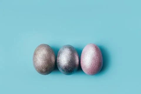 Three colored chicken eggs of pink, silver, golden on blue color background Photos
