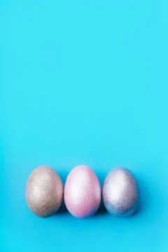 Three colored chicken eggs of pink, silver, golden on blue color background Photos