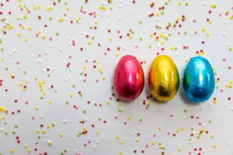 Three colored chocolate easter eggs on white background and colorful confetti Stock Photos