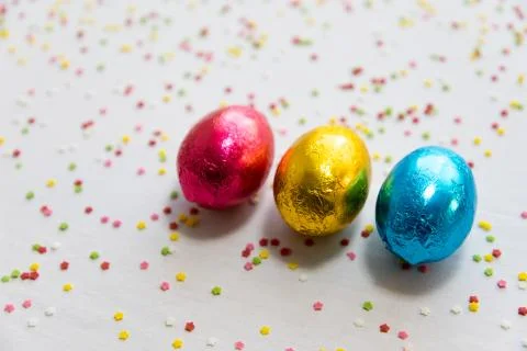 Three colored chocolate easter eggs on white background and colorful confetti Stock Photos